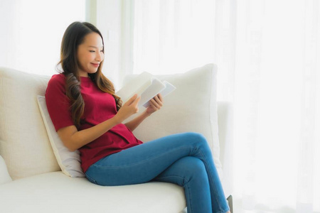 美丽的亚洲年轻女性在沙发椅上看书