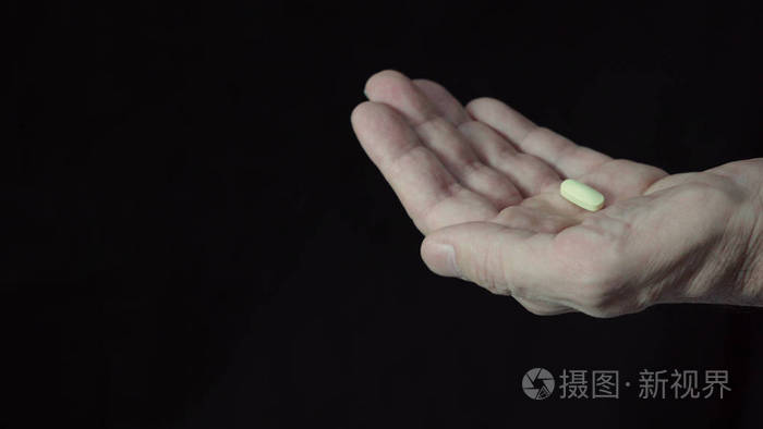 黑色背景下手持一颗药丸的男性手的特写镜头
