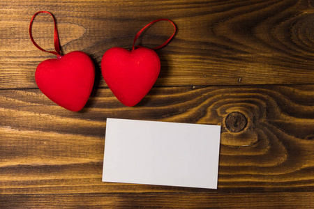 情人节空白贺卡和木质背景上的两颗红心。俯视图，复制空间