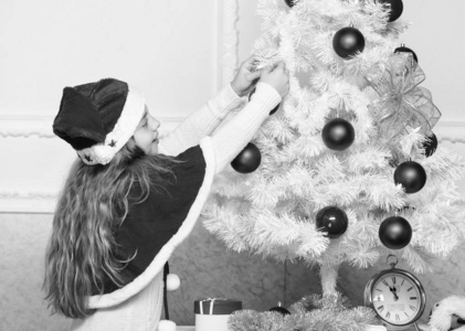 小女孩在装饰圣诞树。珍爱的节日活动。戴圣诞帽的孩子装饰圣诞树。家庭传统观念。孩子们用红球装饰圣诞树