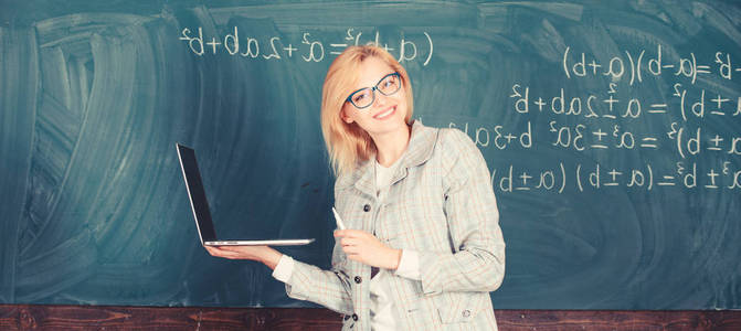 用简单的方法学习。女教师戴眼镜手持笔记本电脑上网。有现代笔记本电脑上网黑板背景的聪明的教育家。数字技术概念