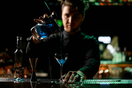 专业调酒师通过过滤网将酒精饮料从量杯倒入玻璃杯