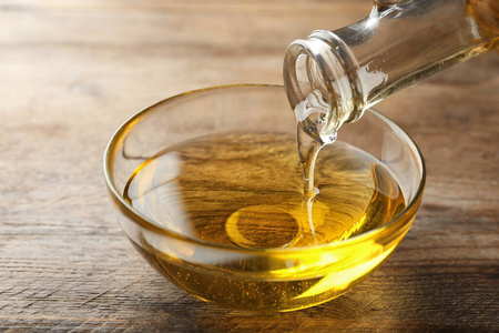 把食用油从罐子里倒进木桌上的碗里照片