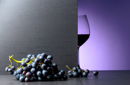 Red wine grapes on a black table and glass of red wine. 