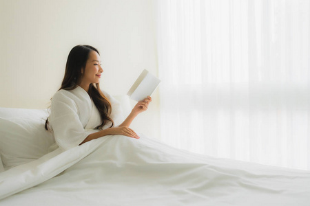美丽的亚洲年轻女性在床上看书