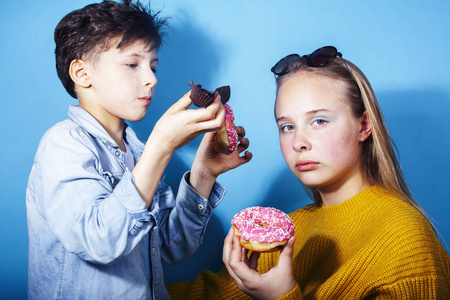 快乐的家庭兄弟姐妹吃甜甜圈的蓝色背景，生活方式的人的观念，男孩和女孩吃不健康的食物