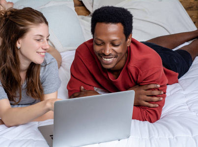 年轻夫妇在家里的床上用笔记本电脑。