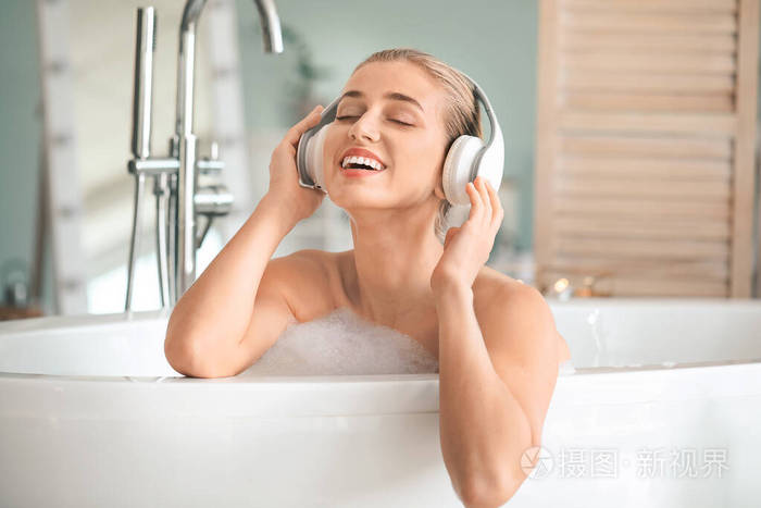 漂亮的年轻女人在浴室里听音乐