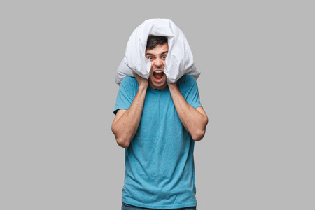 一个穿着蓝色t恤的男人用一个白色枕头捂着头,因为睡觉时害怕看到怪物