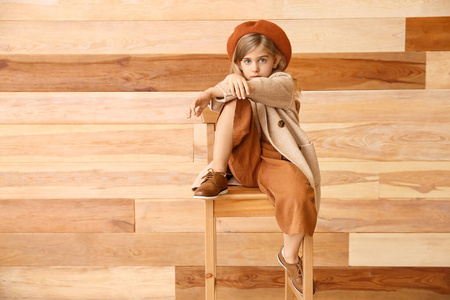 可爱的小女孩穿着秋天的衣服坐在木墙上照片