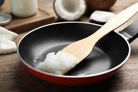 Frying pan with coconut oil and wooden spatula on wooden table. 