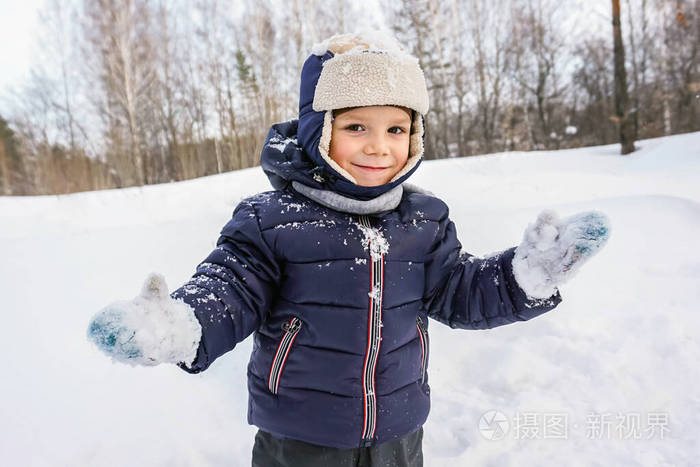 一个快乐的小男孩在雪堆的衬托下在寒冷的冬天雪花在空中飞舞