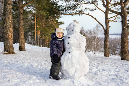 小男孩在冬天玩雪人。冬季与孩子们一起积极户外休闲。戴着温暖帽子，手戴手套的孩子