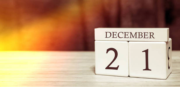 日历提醒事件概念。带有数字和月份的木制立方体，12月21日有阳光。