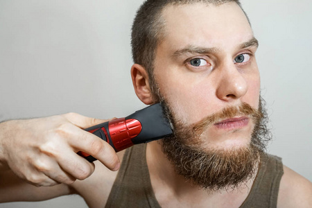 一个留着胡子的家伙在一个孤立的背景上用剪子剪胡子头发和胡子
