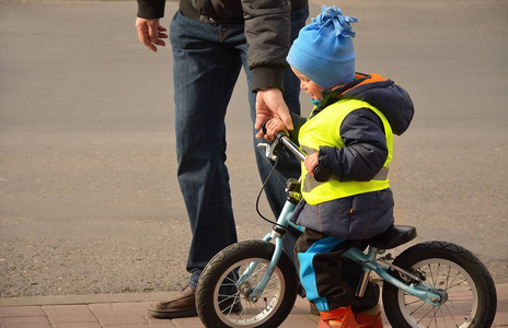 Boy is learning to ride a bike with his dad on the pavement near