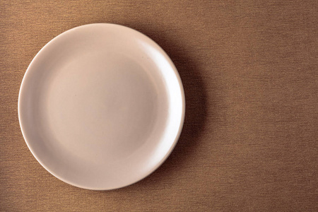 Empty ceramic round beige plate on a beige tablecloth.