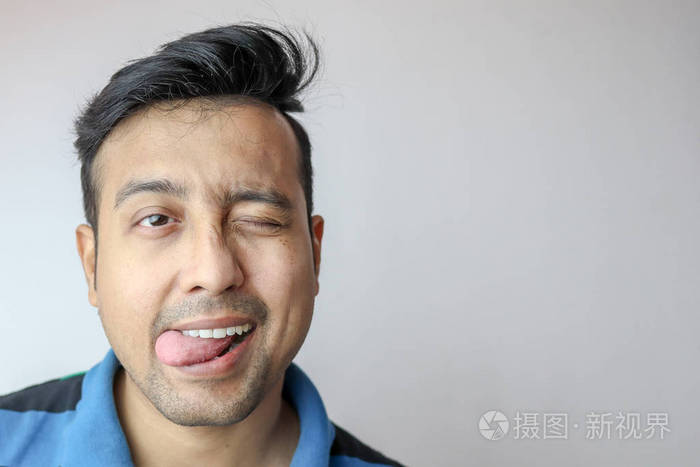 一个年轻的印度男性眨眼舌头伸出嘴脸上有一个有趣的调皮调皮的表情