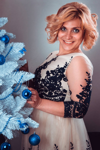 年轻快乐的女人穿着优雅的晚礼服，拿着玩具站在圣诞树旁