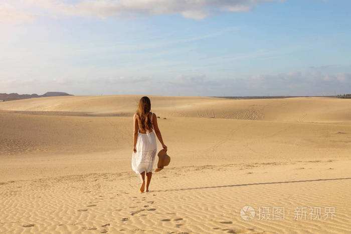 夕阳西下，身穿白色连衣裙的年轻美女在沙漠沙丘上散步。走在科拉雷乔杜纳斯Corralejo Dunas的金色沙滩上的女孩。