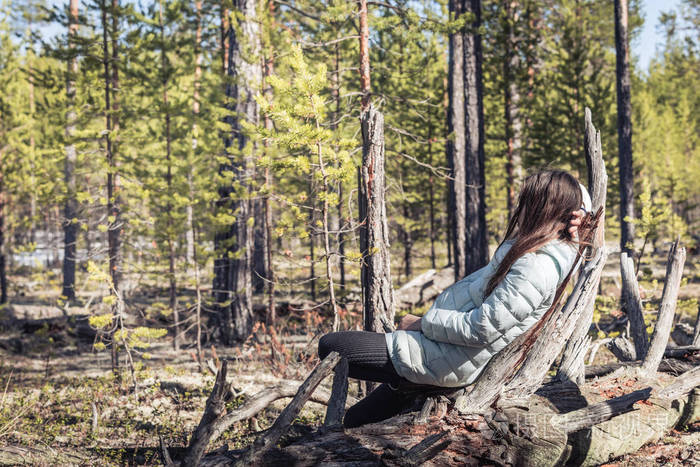 徒步旅行后穿着轻便夹克的疲惫女孩躺在松林中的老树桩上休息