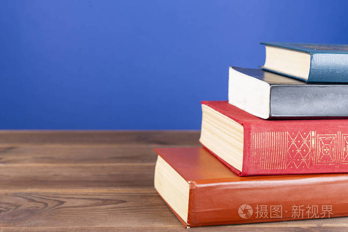 简单的组成,许多精装书,彩色书籍在一个木桌子上和一个明亮的蓝色背景