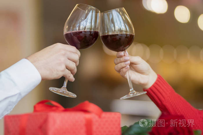一对夫妇坐在餐馆里把酒杯交叉在一起桌上有一个礼品盒和一朵美丽的