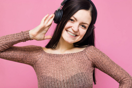 一个快乐的年轻美丽的女人在粉红色的墙壁背景下独自摆好姿势，用耳机听音乐