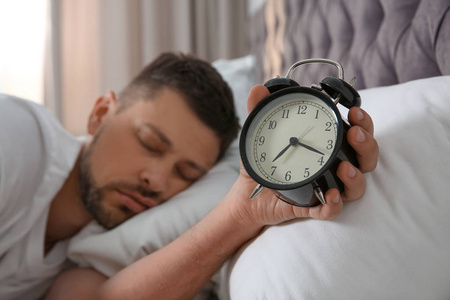 男人早上带着闹钟在家睡觉，注意力集中在手上