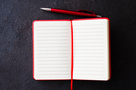 Empty red notebook with red pen on dark background. Blank paper 