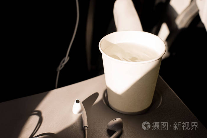 飞机上折叠桌上的白纸水杯和耳机在飞机上喝酒飞行中脱水皮肤水合作用