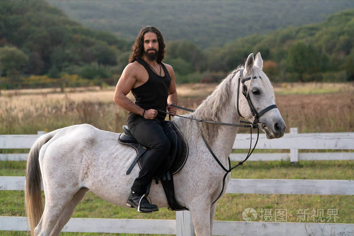 一个英俊的大胡子男人在农场骑马.