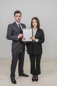 一对成功的生意人站在一起，面带自信的表情，手里拿着一张空白的空白纸做的剪贴簿。