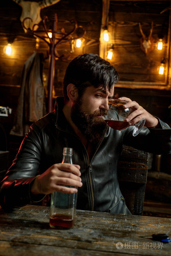 有胡子的男人拿着玻璃白兰地有男子气概的喝酒除味品尝英俊的胡子男人