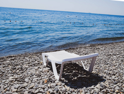 躺椅是白色的，坐落在海岸边的一个多石的海滩上。海边躺椅