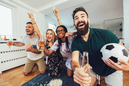 Group of cheerful friends watching soccer match and celebrating 