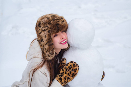 冬季雪地花园里年轻美女的画像堆雪人。快乐女人冬季肖像。冬天快乐。