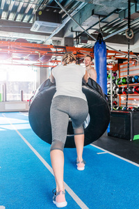 Fit female athlete working out with a huge tire, turning and fli