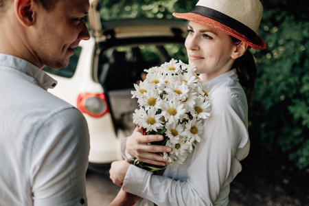 年轻幸福的情侣穿着白色T恤，在车旁玩得开心，周末在城外，假期和公路旅行的概念