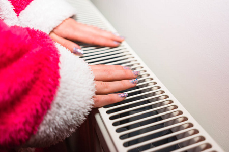 Closeup of a woman warming up her hands on a white radiator at 