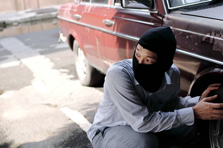 蒙面小偷穿着黑色的巴拉克拉瓦试图闯入汽车.犯罪概念.照片