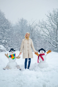 冬天雪地花园里滑稽女孩的画像堆雪人。雪林里的雪人。阳光明媚的冬日，快乐的微笑女孩堆雪人。