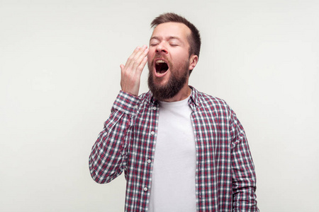 Portrait of tired bearded man yawning widely and covering mouth 