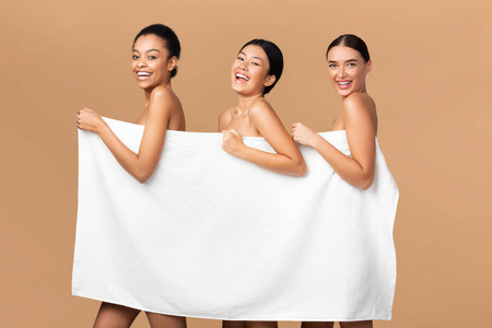 三个女孩拿着白毛巾微笑着在米色背景上摆姿势