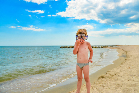 一个戴着潜水眼镜的男孩站在海边。