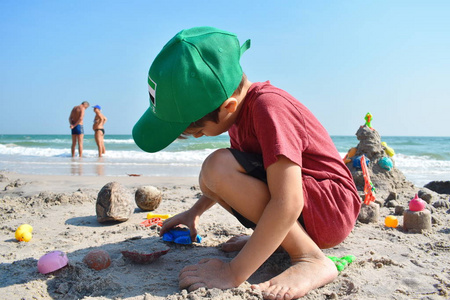 一个男孩在沙滩上玩。这孩子造沙雕。海滩上的玩具。海滨假日快乐。