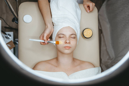 美容师用刷子将藻酸盐面膜涂在一位女士的脸上。