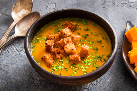 黑色陶瓷碗中的纯素南瓜汤,背景为深色,俯视图照片