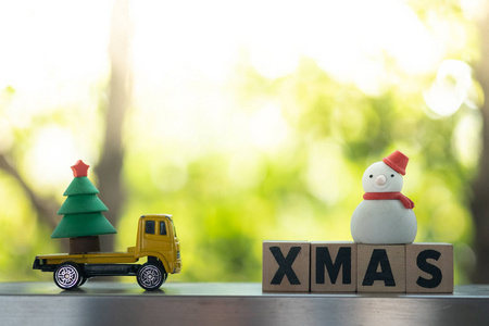 Toy yellow car carries a Christmas tree sent to snowman on wood 