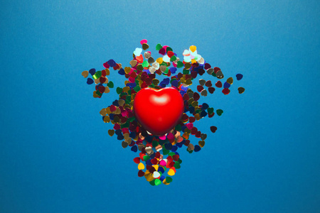 Decorative red heart with colorful confetti on blue background. 